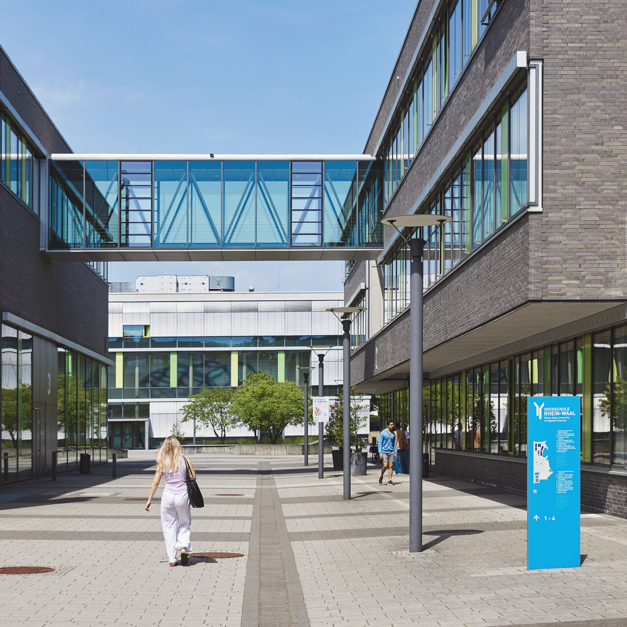 Campus Kamp-Lintfort: Rechts und links ein modernes Gebäude, das mit einer Brücke aus Glas verbunden ist.